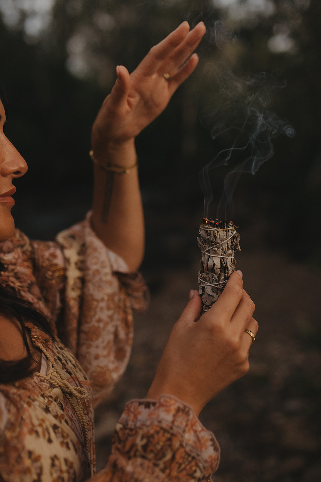 Close-up of Charlene's hands holding a smoking sage bundle during a ceremonial smoke cleansing ritual, symbolising energetic clearing and the sacred pause before healing.