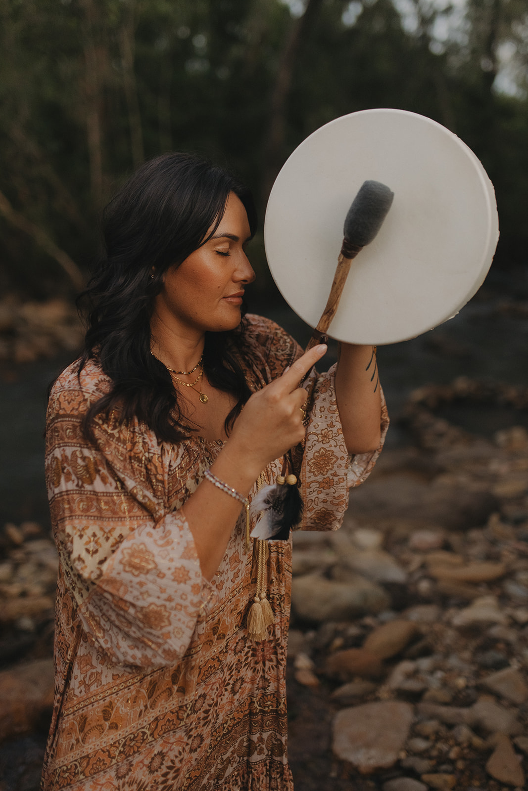 Charlene holding a shamanic drum near a rocky creek in Sarina QLD during a sacred energy healing session focused on releasing emotional clutter and restoring balance.