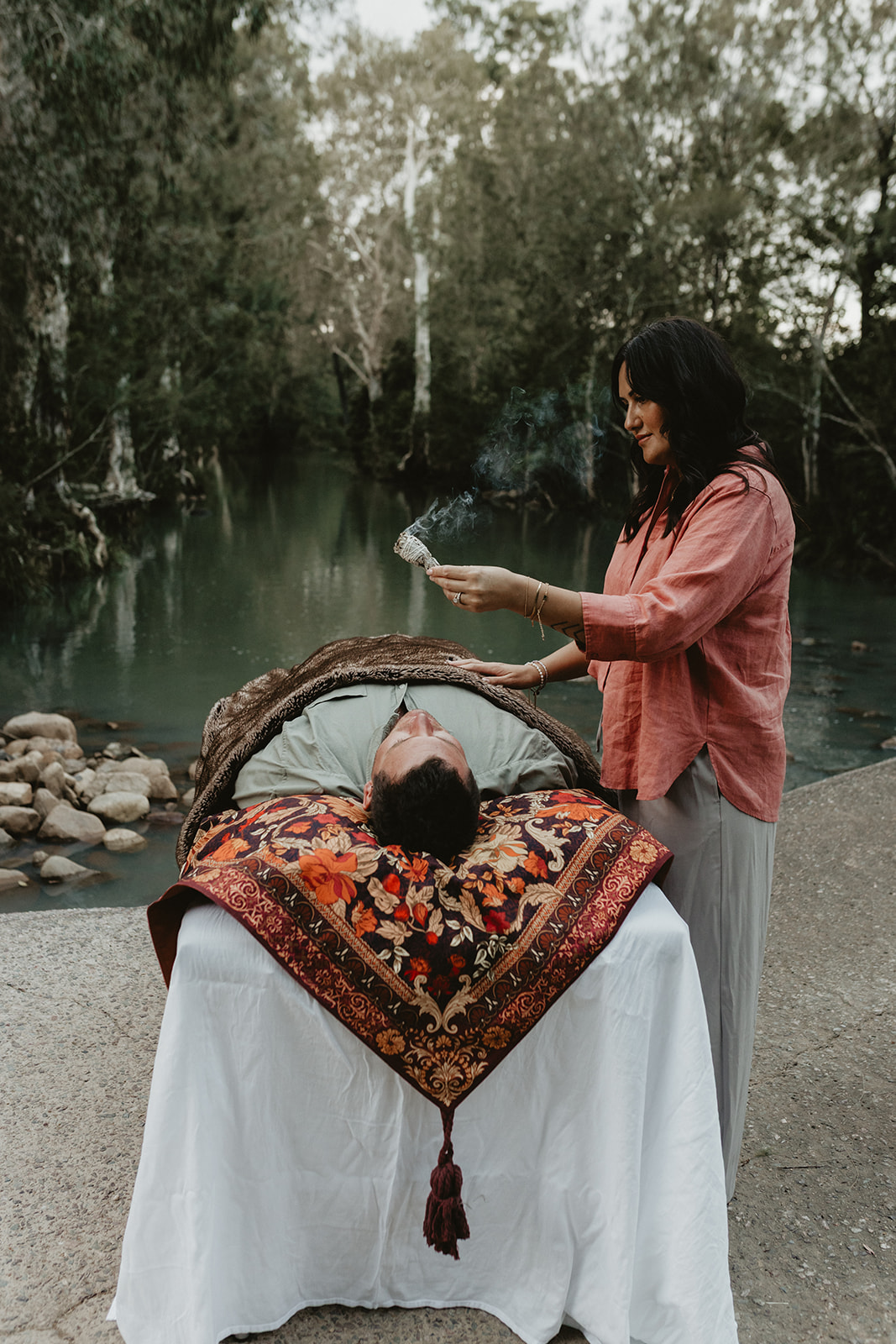 Charlene offering a sacred energy healing session by the water in Sarina QLD using smoke cleansing and intuitive guidance to support emotional release and nervous system regulation.
